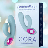 A box titled "Femme Funn Cora Rabbit Vibrator - Light Blue" features an image of the product depicting a light blue, ergonomic vibrator with pink accents. The background is blurred with pastel colors, adding a soft, dreamy effect. Enjoy powerful vibrations and ten vibrating modes with this luxurious device from Femme Funn.